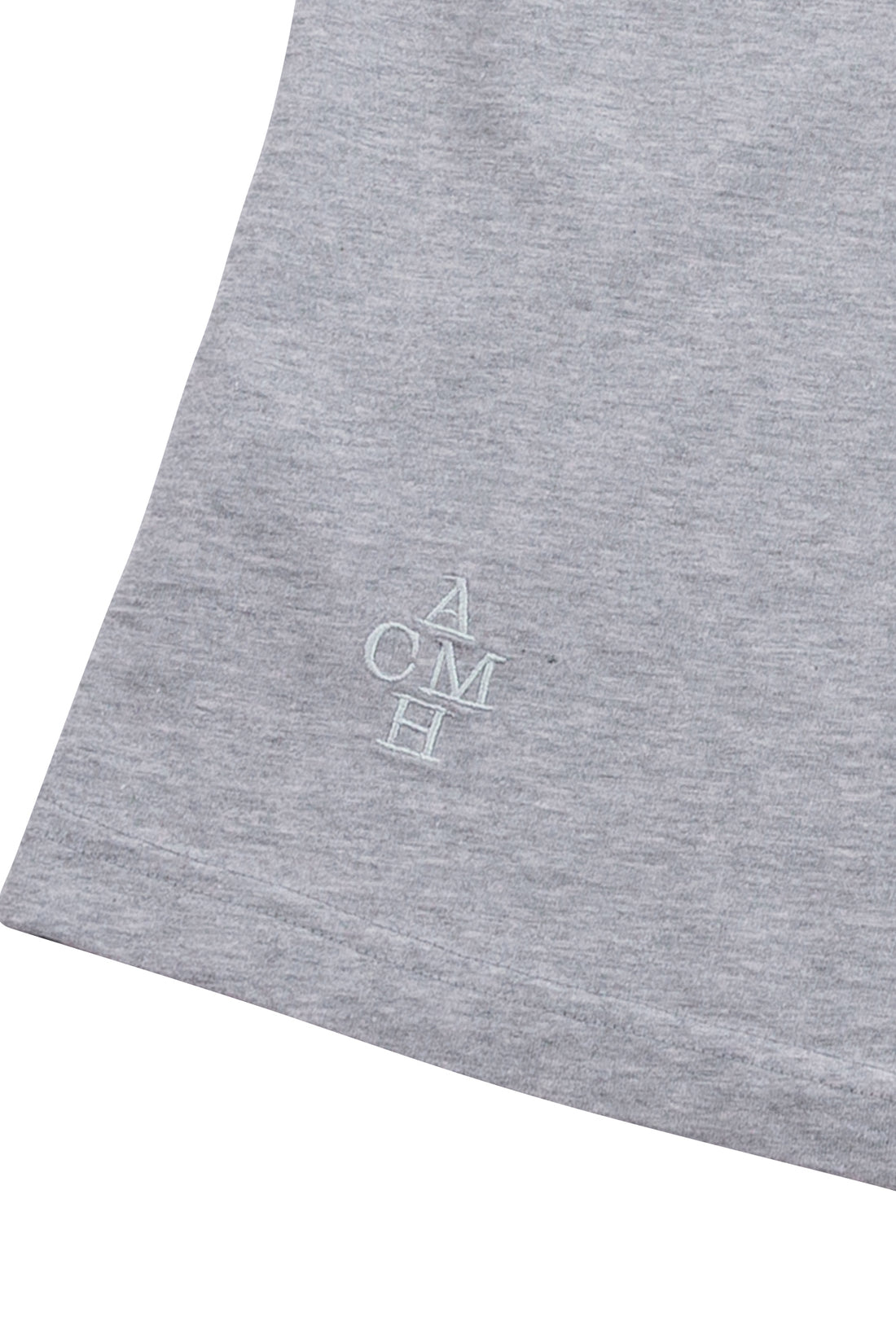 Close-up of a heather gray fabric surface with a small white embroidered monogram reading ACMH near the lower left area.